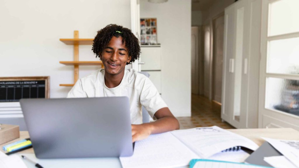 Smiling teen studying at home with a laptop and books, reflecting responsibility from outpatient treatment support.